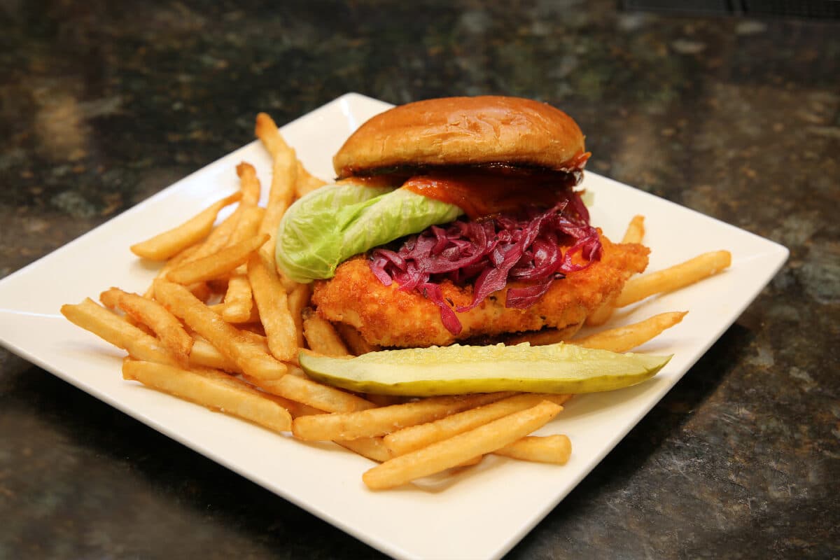 Bavarian Chicken Schnitzel Crunch sandwich with panko breaded chicken, braised cabbage, and paprikash aioli on a brioche bun, served with fries.