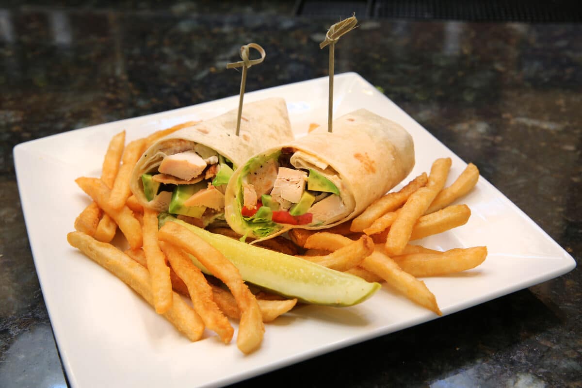 Chicken Chop Wrap cut in half, filled with seared chicken, bacon, avocado, romaine, tomato, and ranch dressing, served with a side of fries.