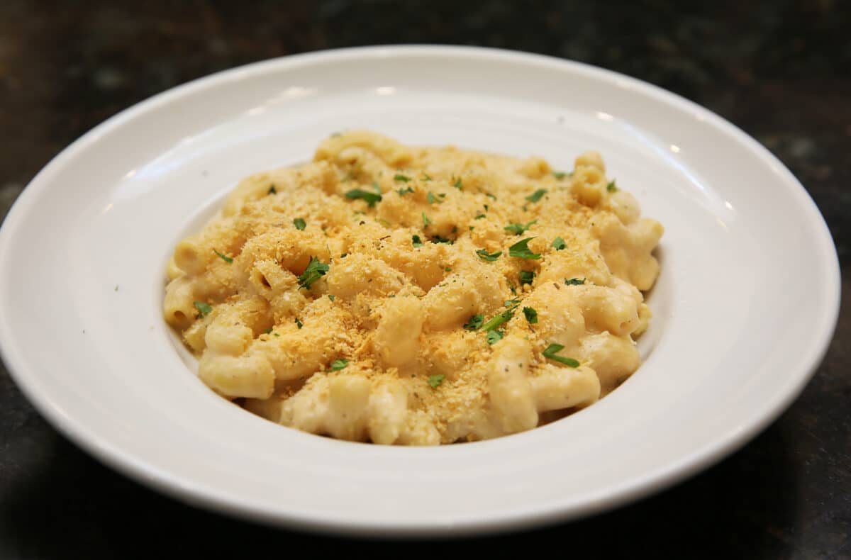 Four Cheese Mac and Cheese featuring jumbo macaroni tossed in house cheese sauce and topped with toasted breadcrumbs.