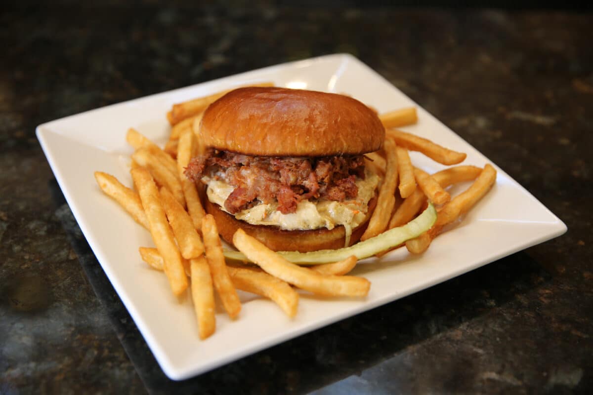 Peach Barbecue Pulled Pork Sandwich on a brioche bun with smoked jalapeño slaw and sweet peach-infused BBQ sauce, served with fries.