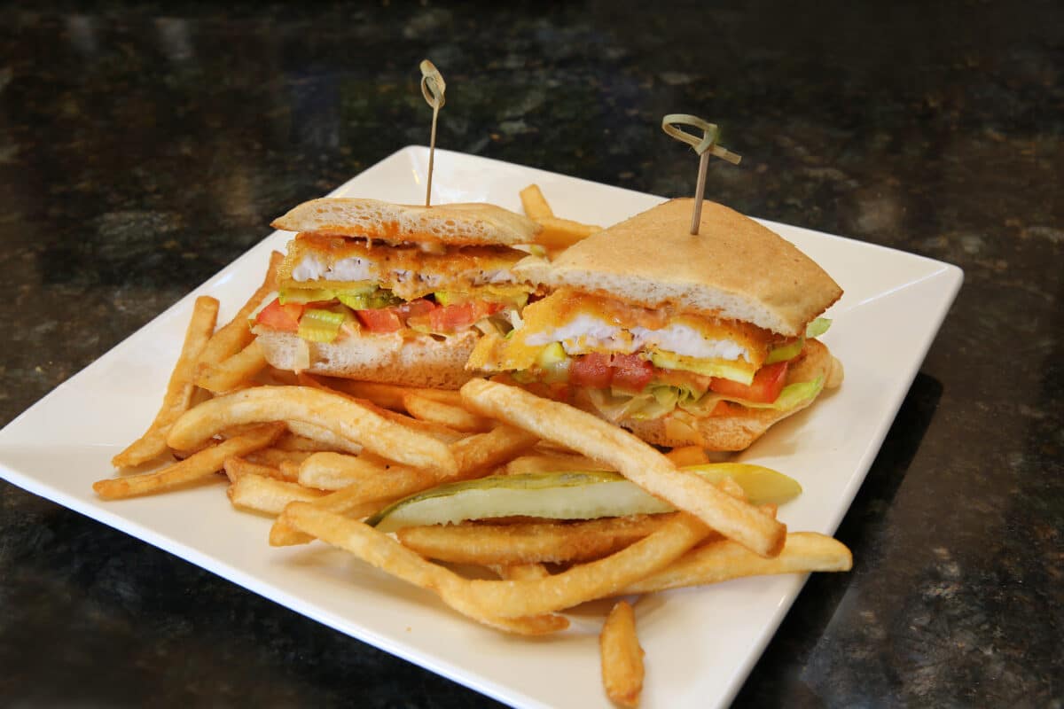 Southern Catfish Po'boy sandwich featuring cornmeal breaded catfish, shaved romaine, tomato, and Cajun remoulade, served with fries.