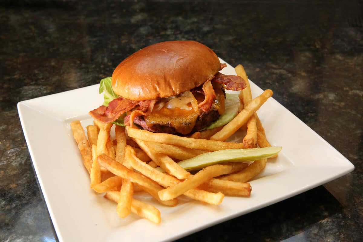 Tavern at Park Signature Burger on a brioche bun with black pepper bacon, bacon jam, beer-braised onions, and medium cheddar cheese.