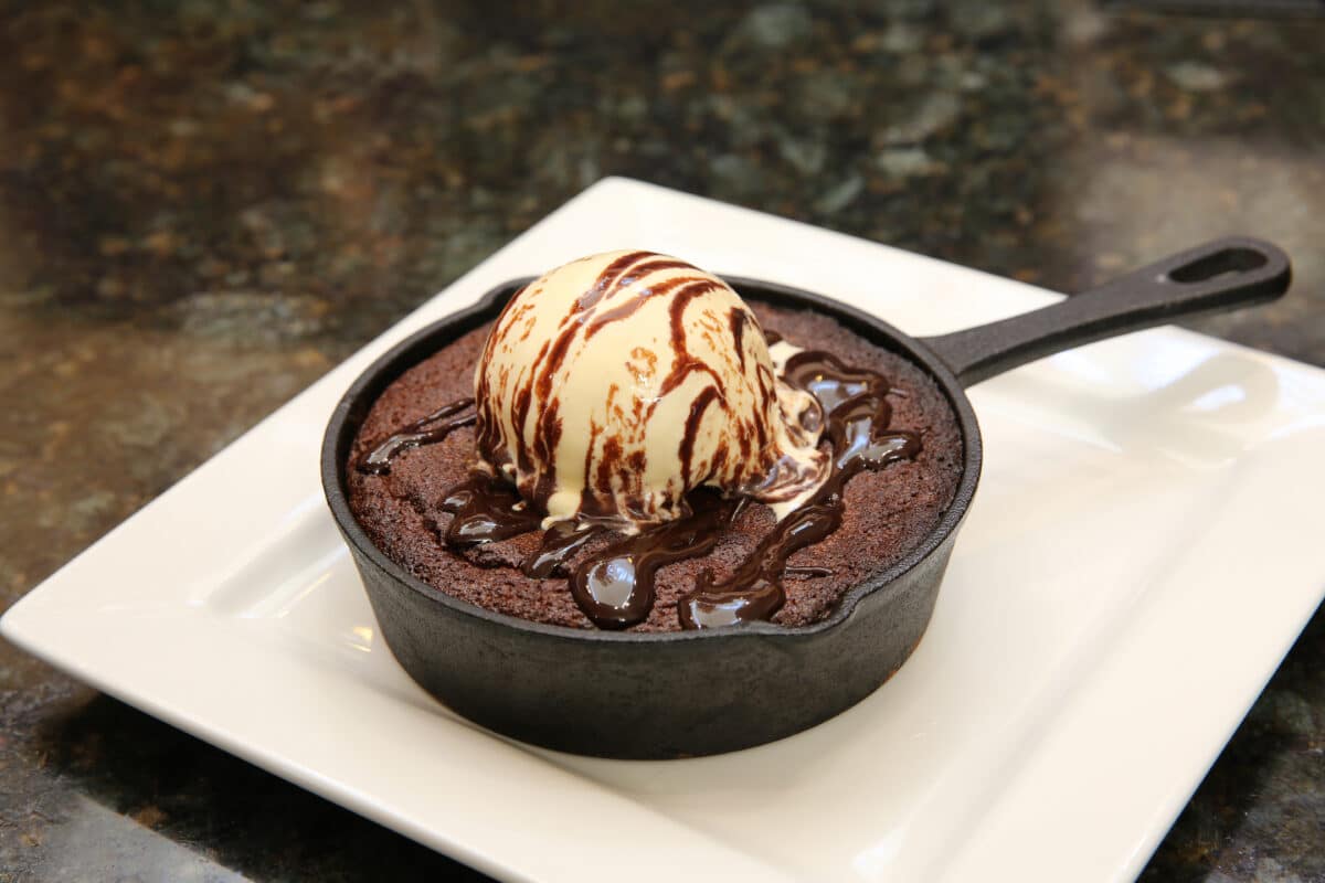 Warm Cast Iron Skillet Brookie (cookie and brownie mix) topped with vanilla ice cream and chocolate sauce, served in a small skillet.